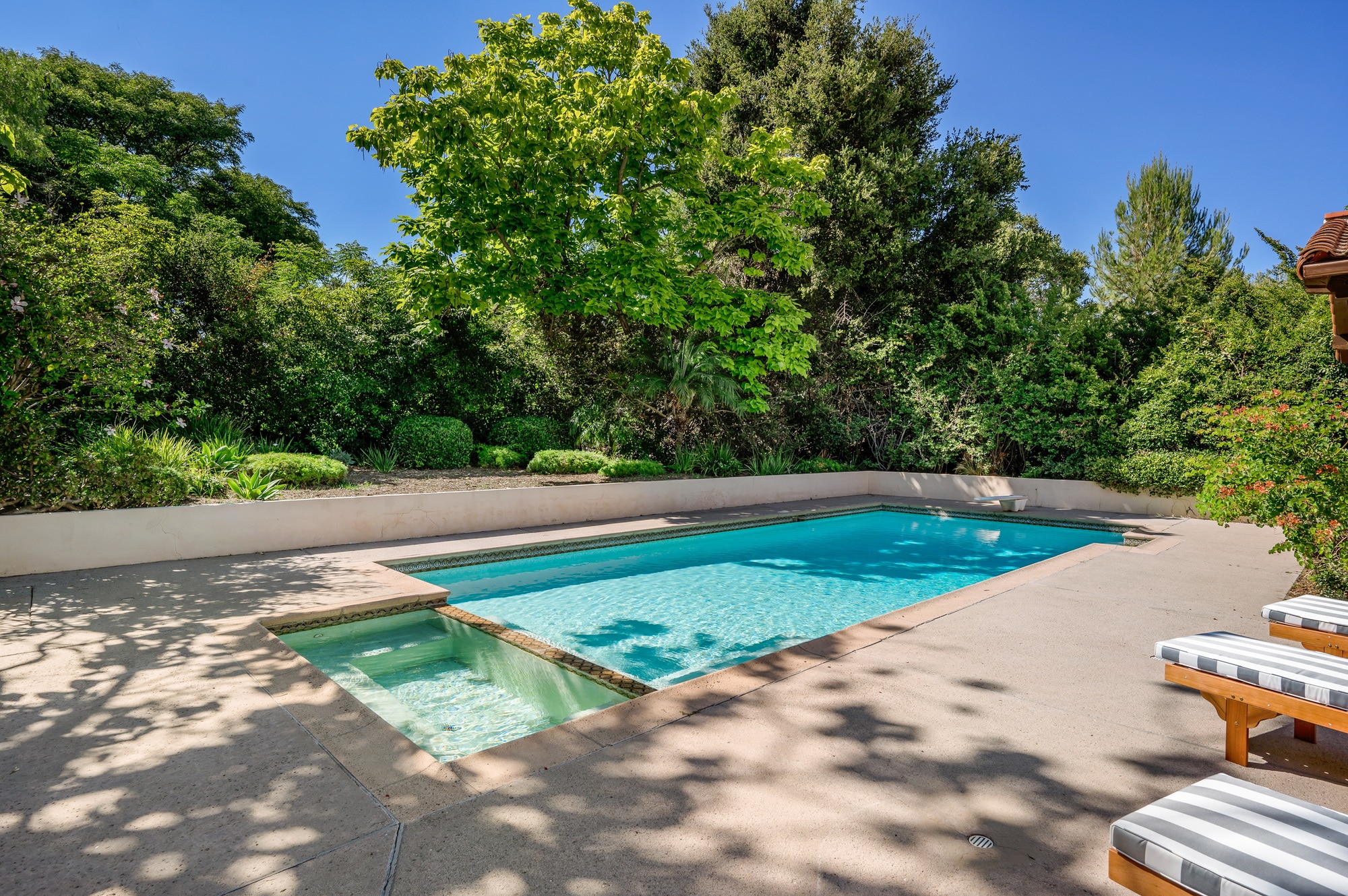 an outdoor pool with two chairs near it and a fence surrounding